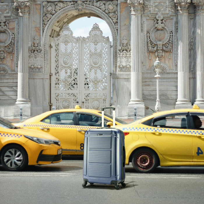 Silver suitcase in front of yellow taxis with an ornate building in the background