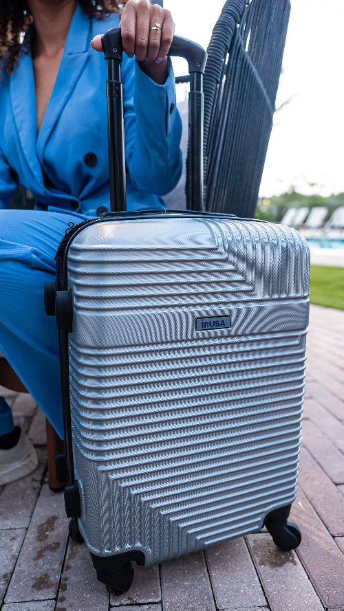 Person holding a silver suitcase with a textured surface, sitting on a chair outdoors.