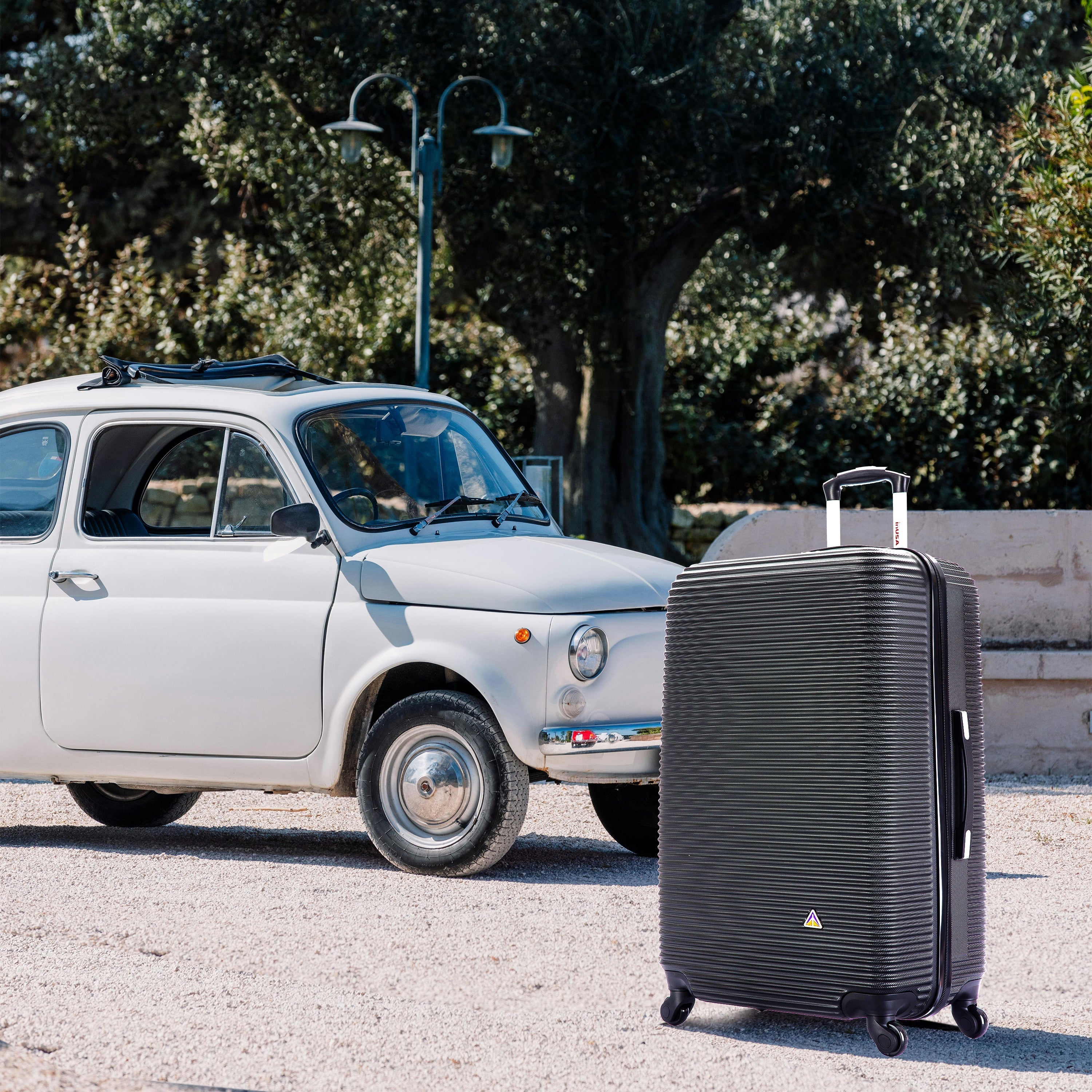 Black suitcase in front of a white vintage car with trees in the background