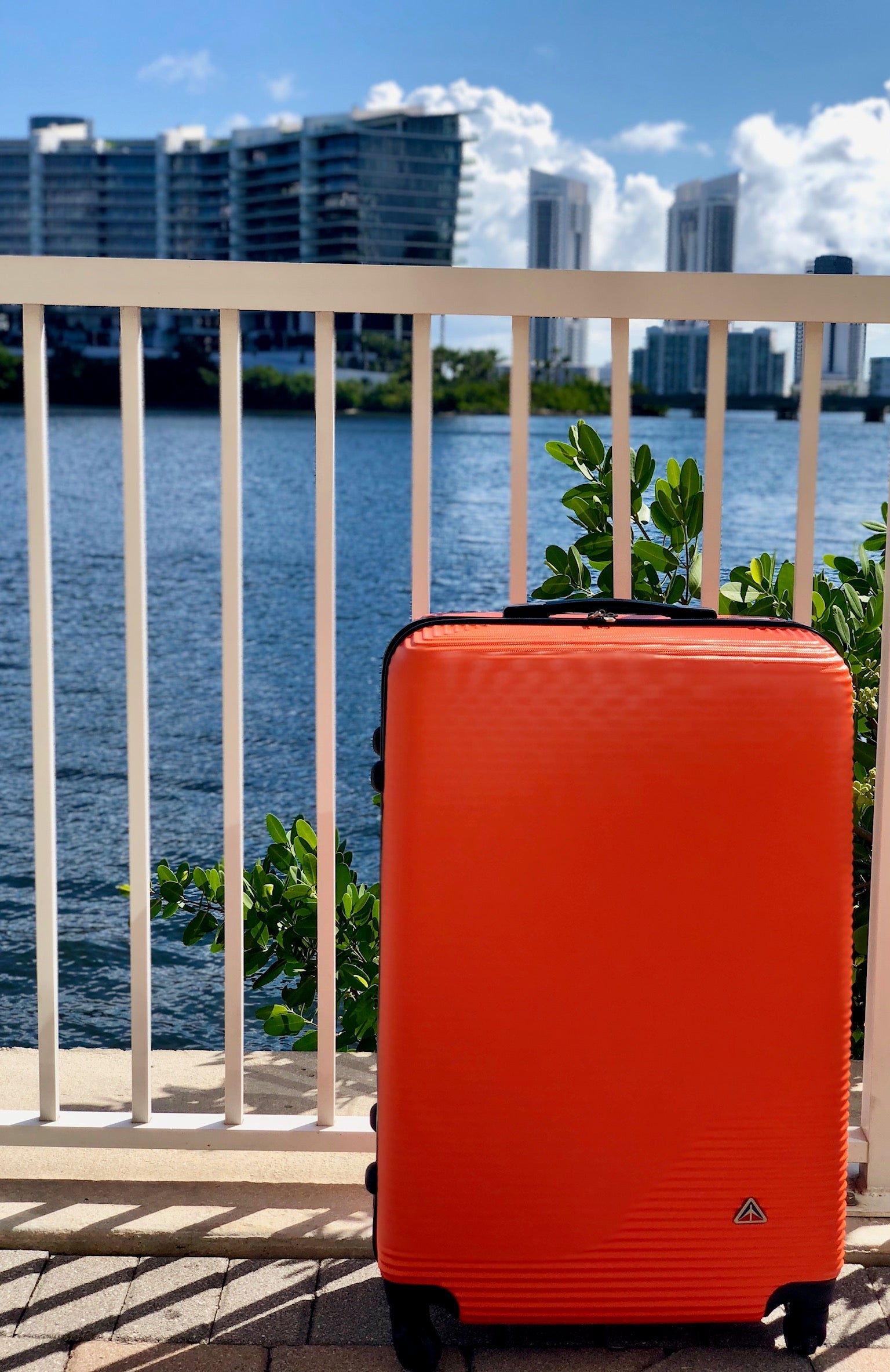Orange suitcase on a balcony with water and buildings in the background