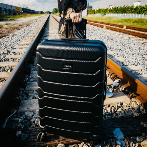 Black suitcase with 'INUSA' branding on a railway track