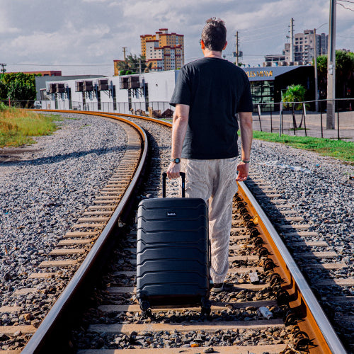 Man with a suitcase walking on train tracks towards an urban landscape
