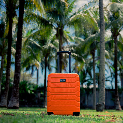 Orange suitcase with a brand logo on a grassy area with palm trees in the background