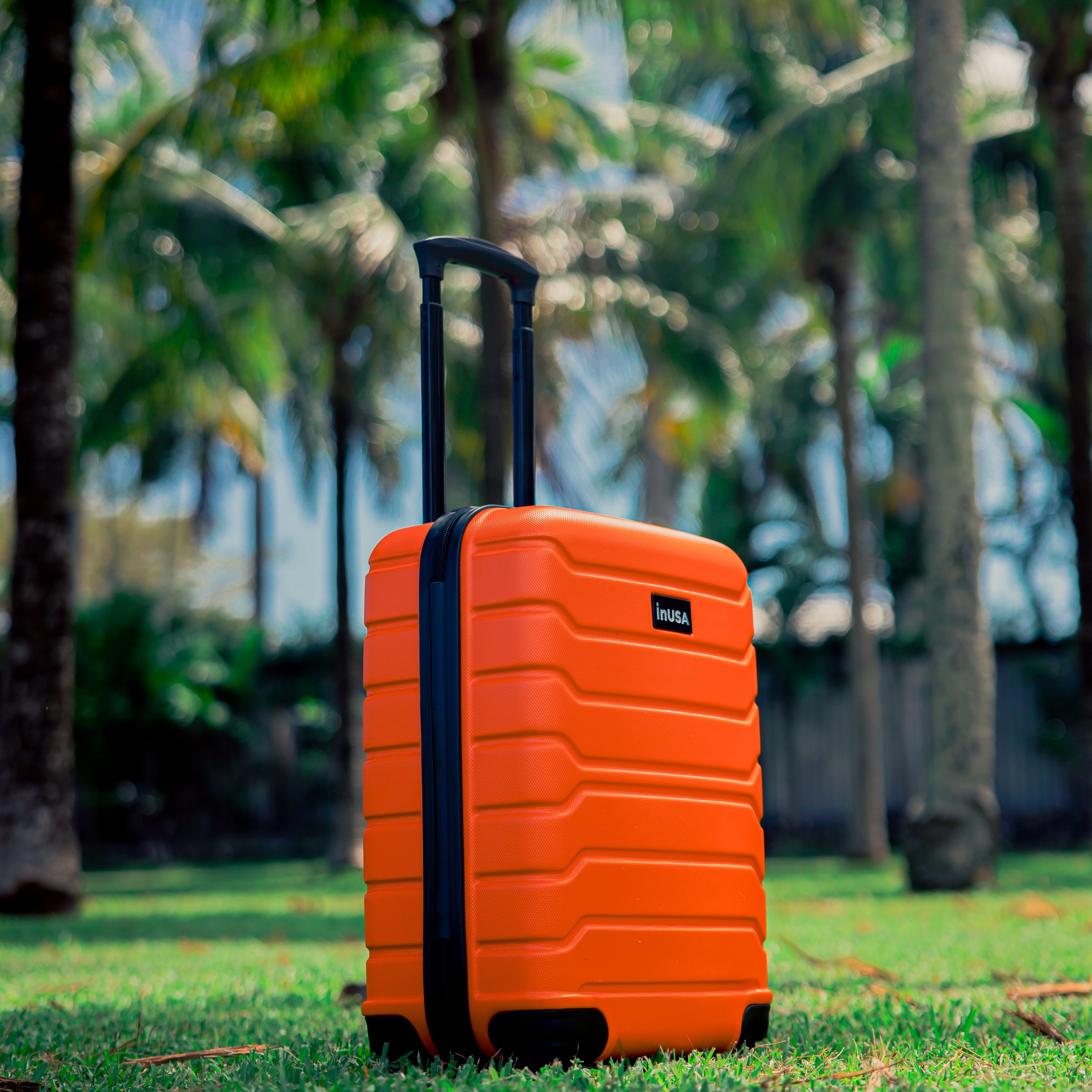 Orange suitcase with black handle on grass with palm trees in the background