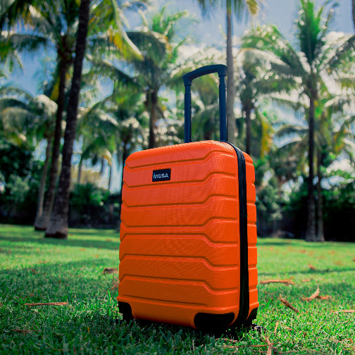 Orange suitcase with a brand logo on grass with palm trees in the background