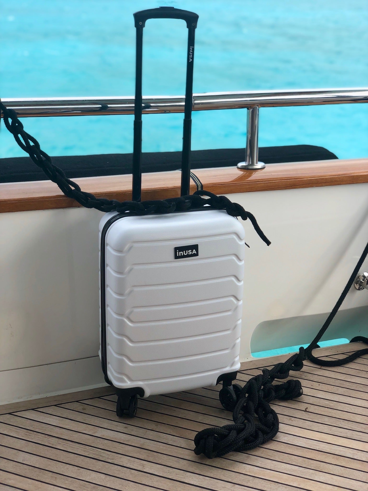 White suitcase with a handle on a boat deck with water in the background