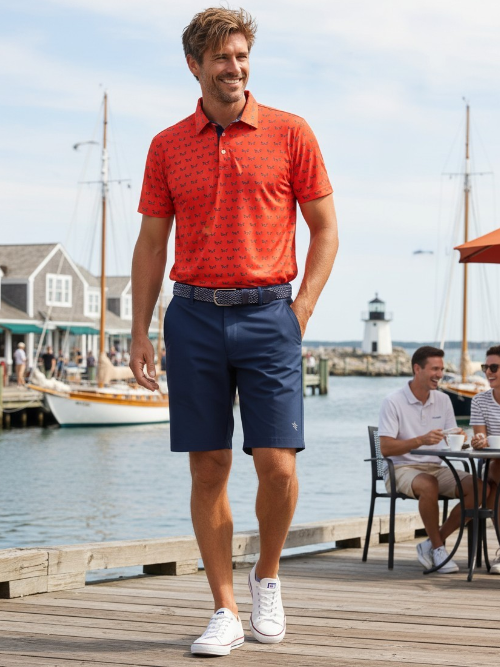 Man in red polo shirt and blue shorts standing on a dock with a harbor background