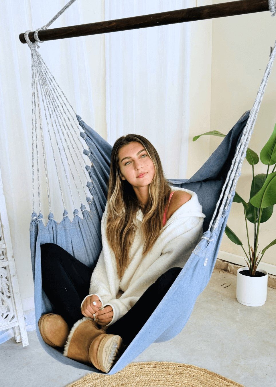Woman sitting in a blue hammock indoors with a plant in the background