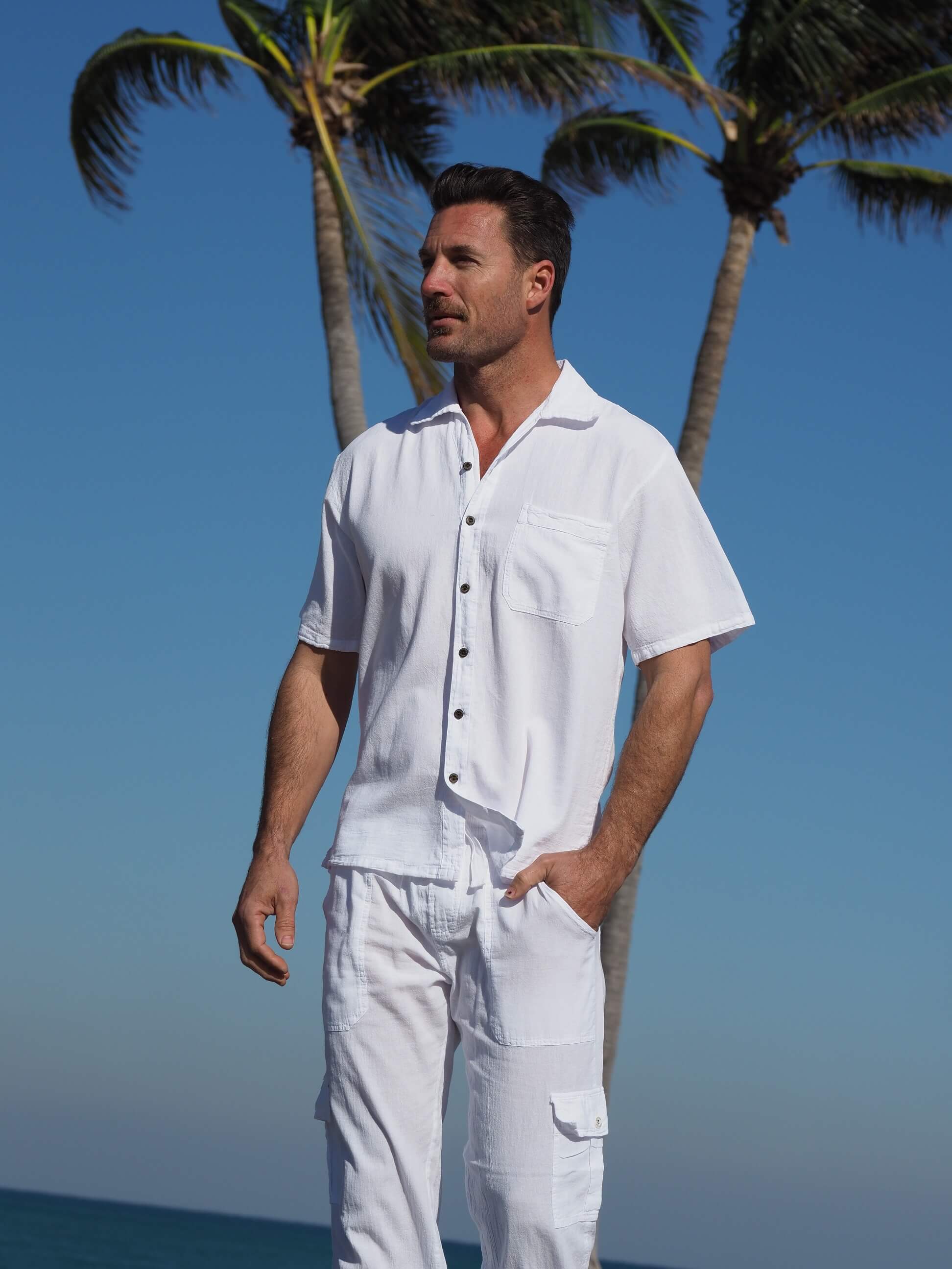 Man wearing a white outfit standing on a beach with palm trees in the background