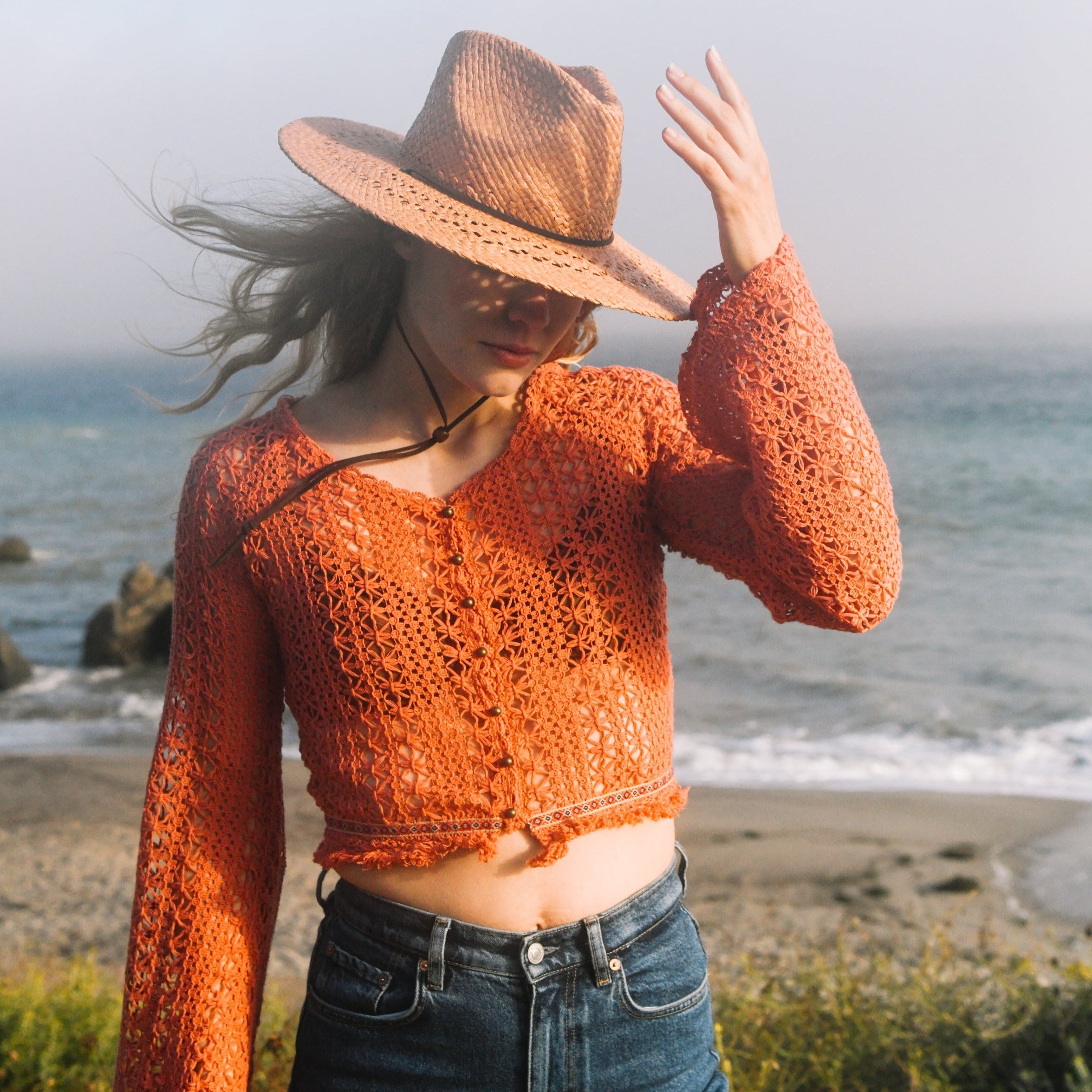 Woman wearing a brown crochet top and hat on a beach