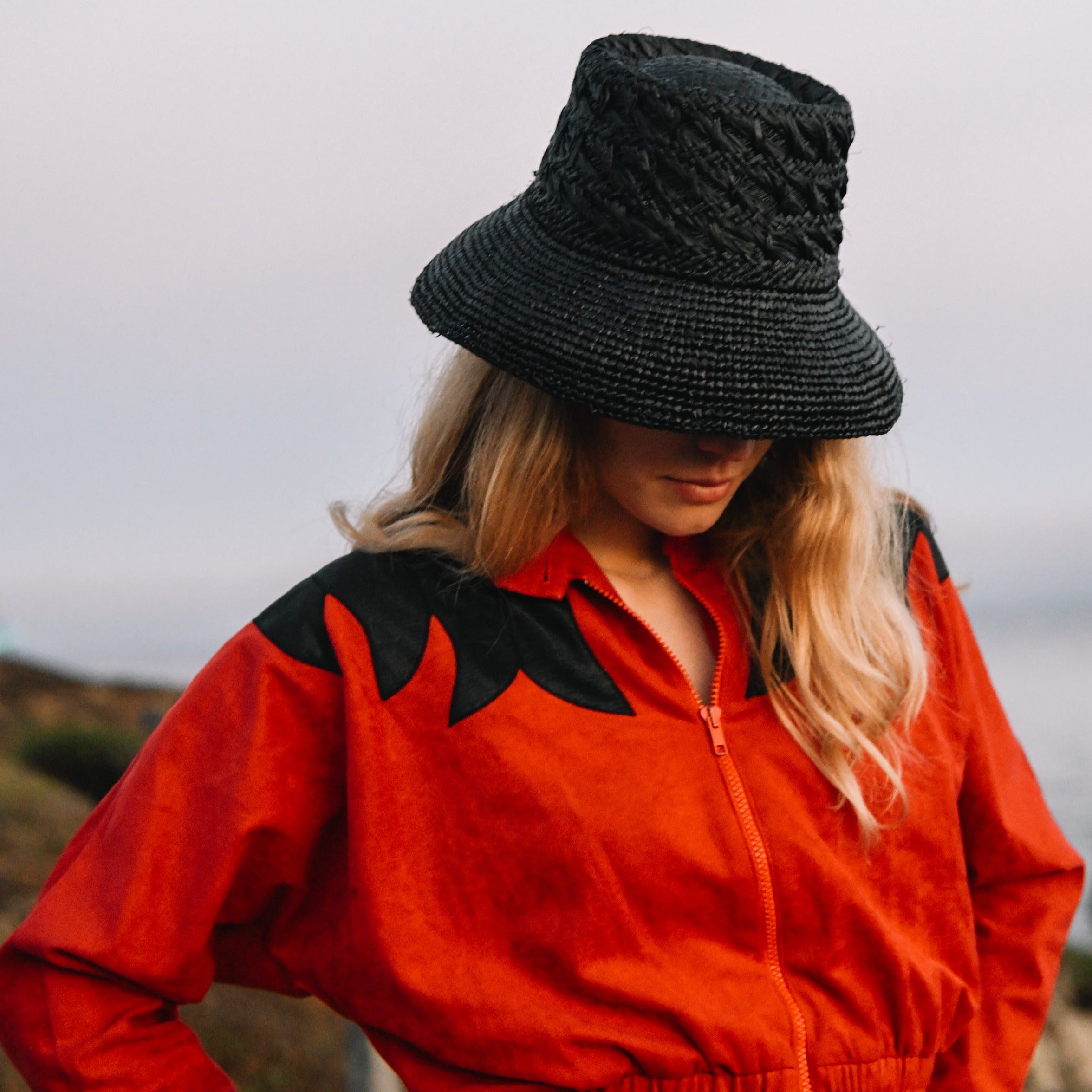 Person wearing a red jacket with black accents and a black hat outdoors.