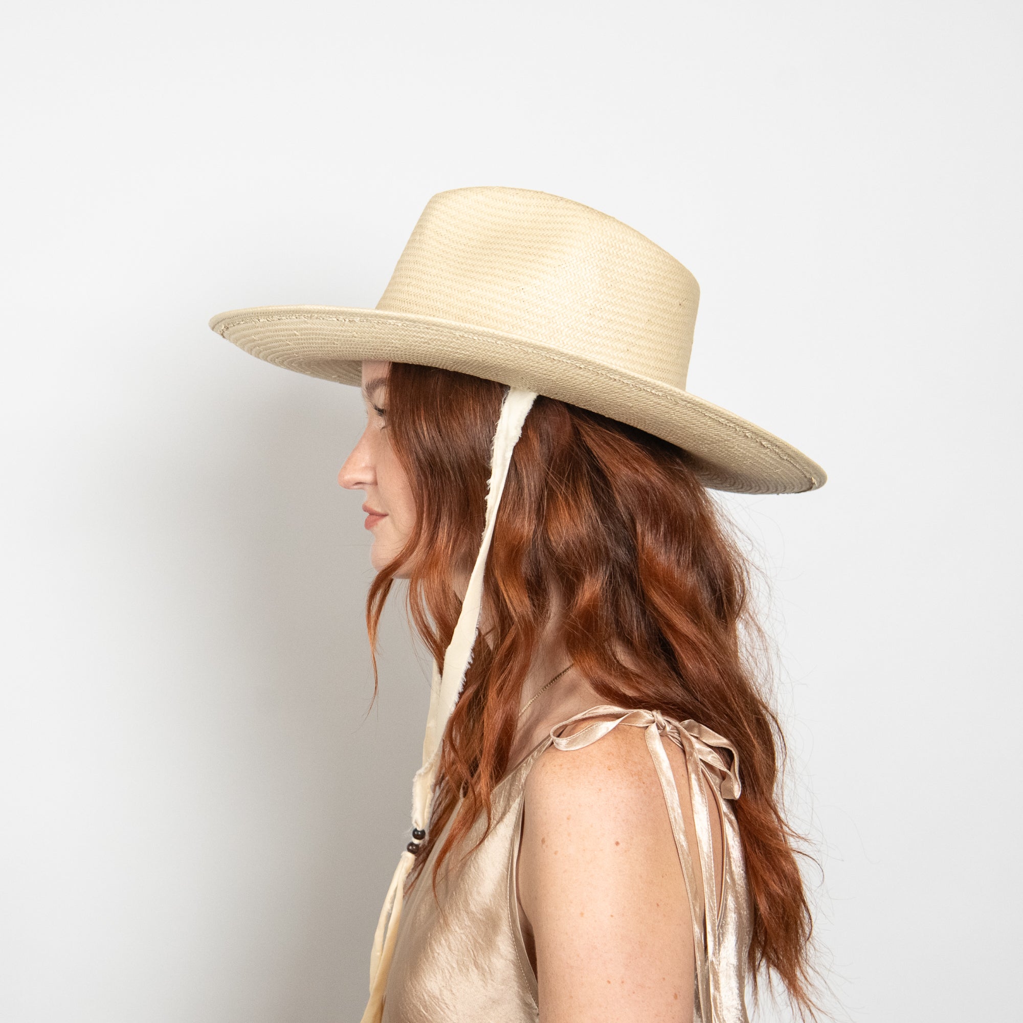 Woman wearing a beige wide-brimmed hat with a ribbon on a light gray background