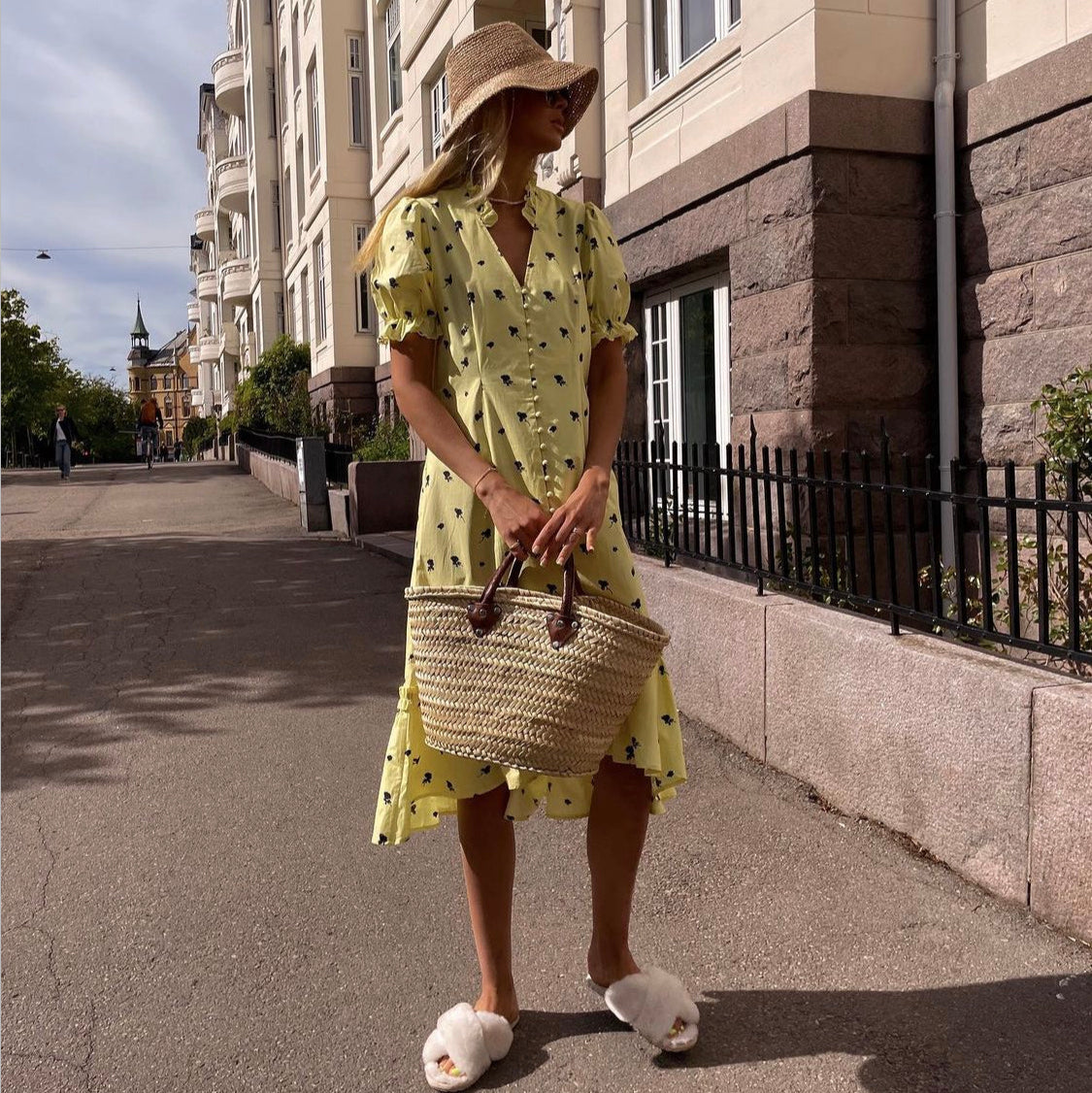Woman in a yellow dress with black patterns walking on a city street.