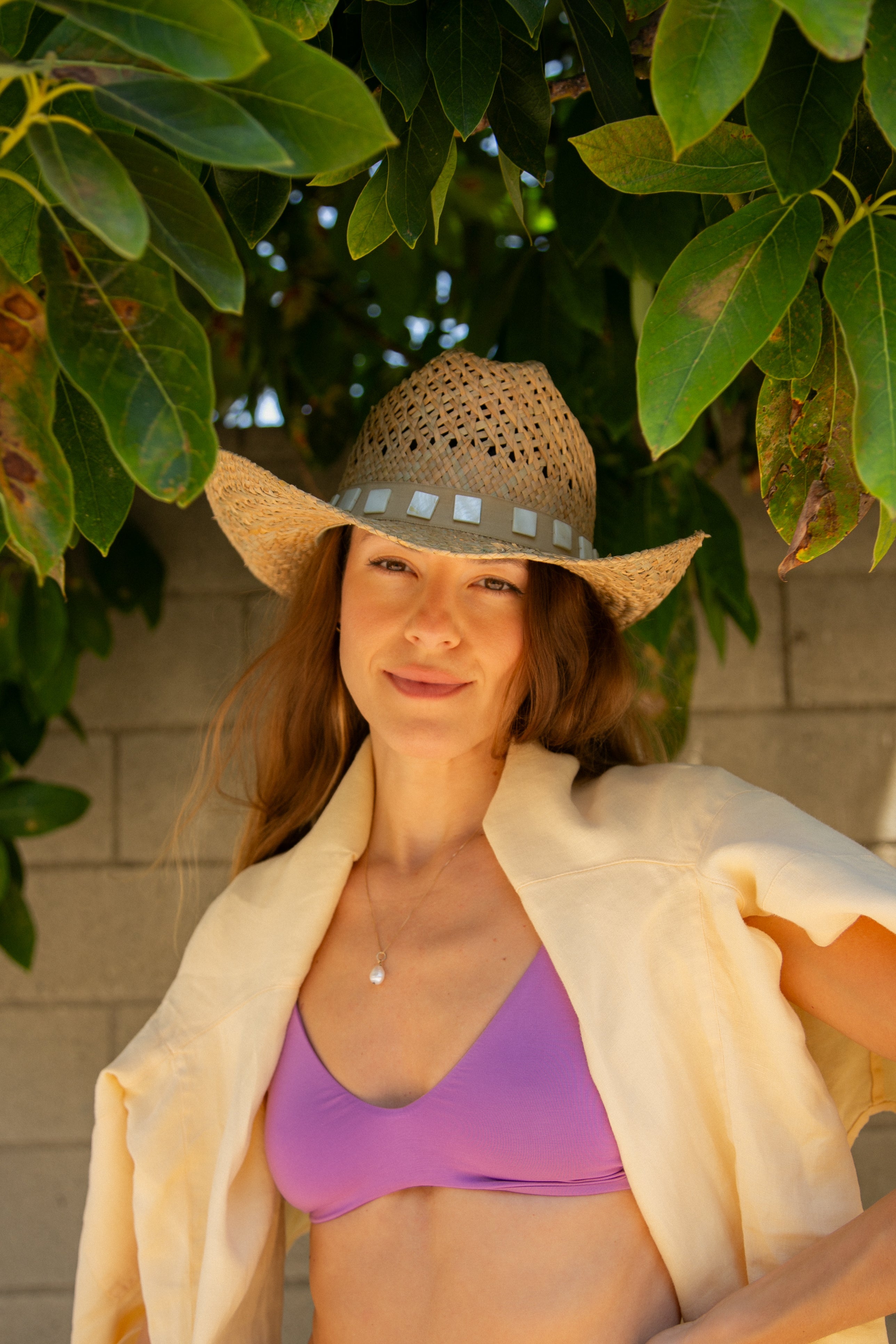 Woman wearing a straw hat and purple bikini top under green leaves
