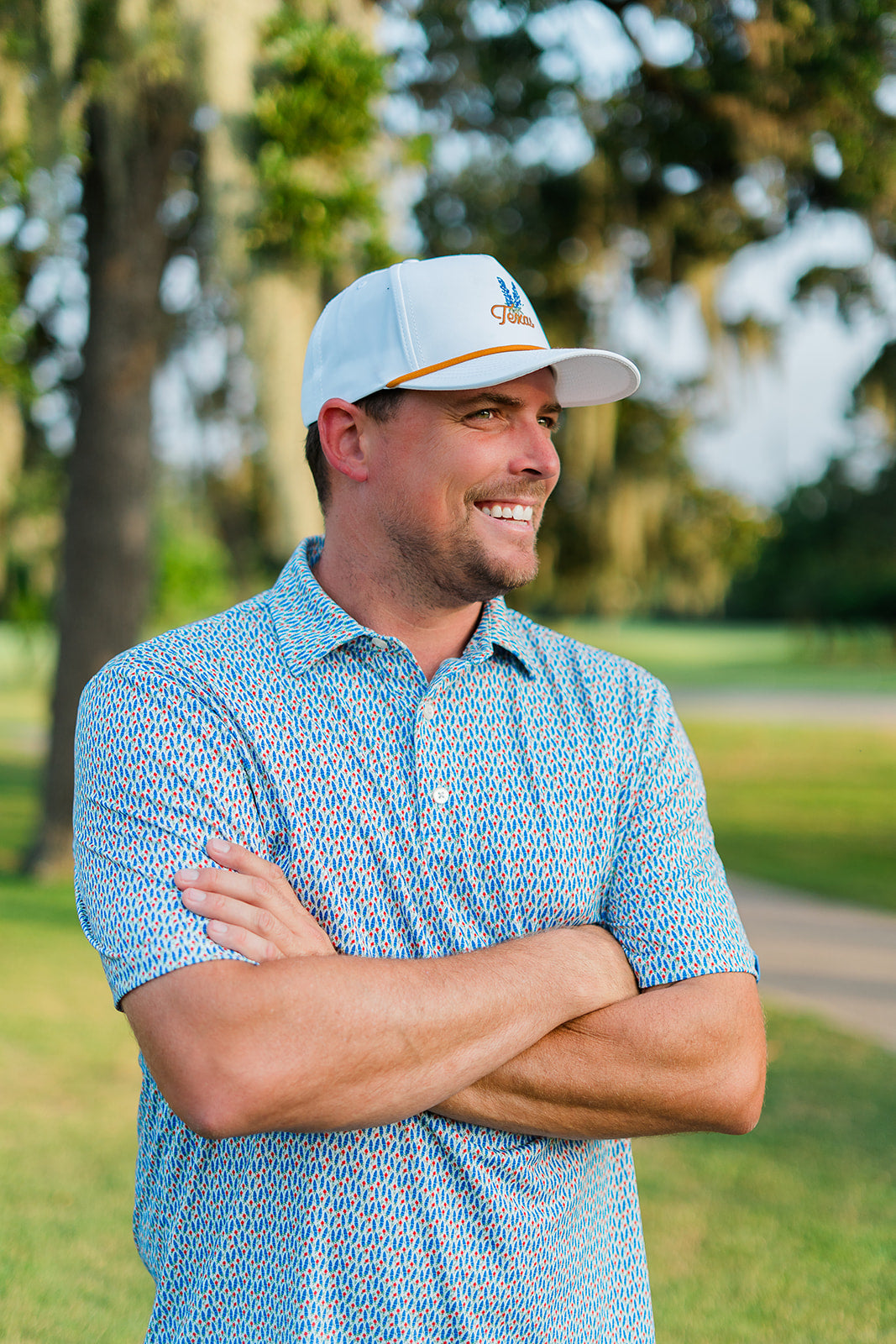 Man wearing a blue patterned shirt and white cap standing on a golf course.