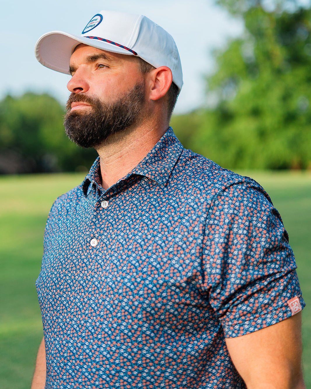 Man wearing a blue patterned shirt and white cap on a golf course