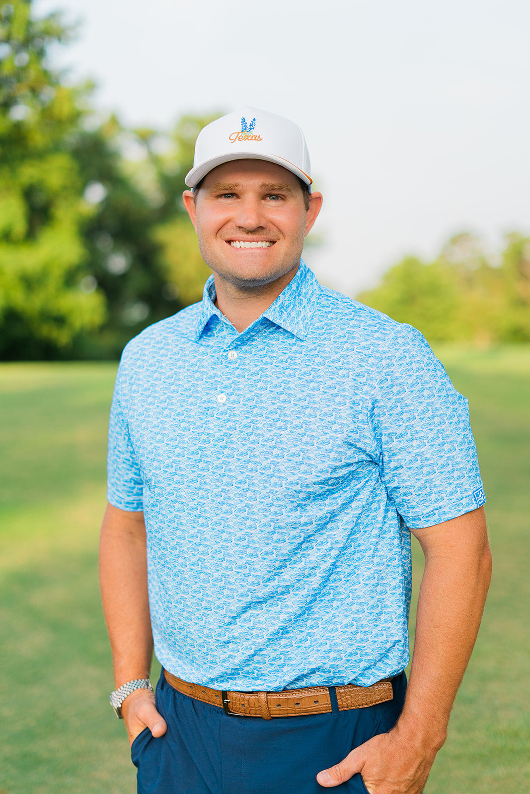 Man wearing a blue patterned polo shirt and white cap on a golf course