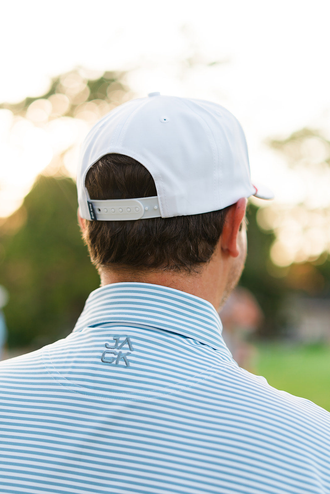 Person wearing a white cap and striped shirt with a logo, standing outdoors.