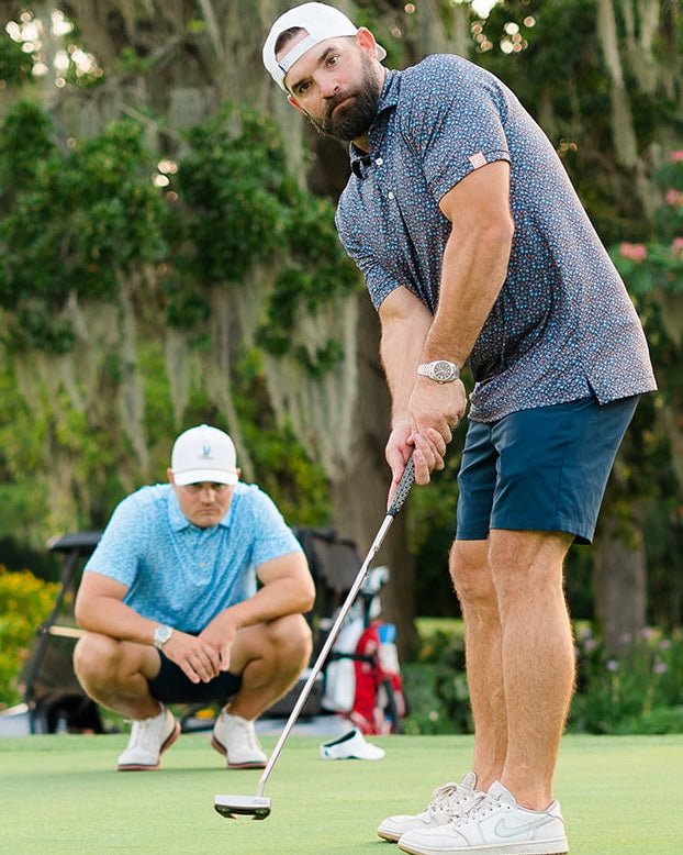 Man playing golf on a green course with another person in the background.