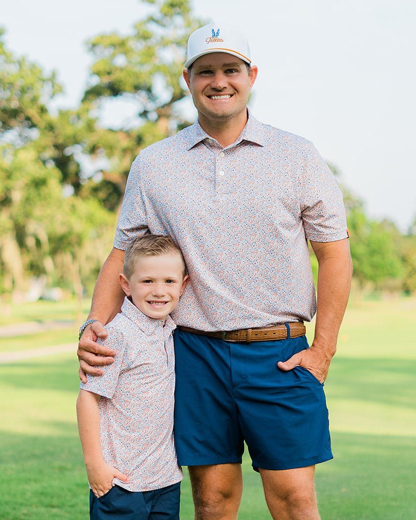 Man and young boy standing on a golf course, both wearing patterned shirts and blue shorts.