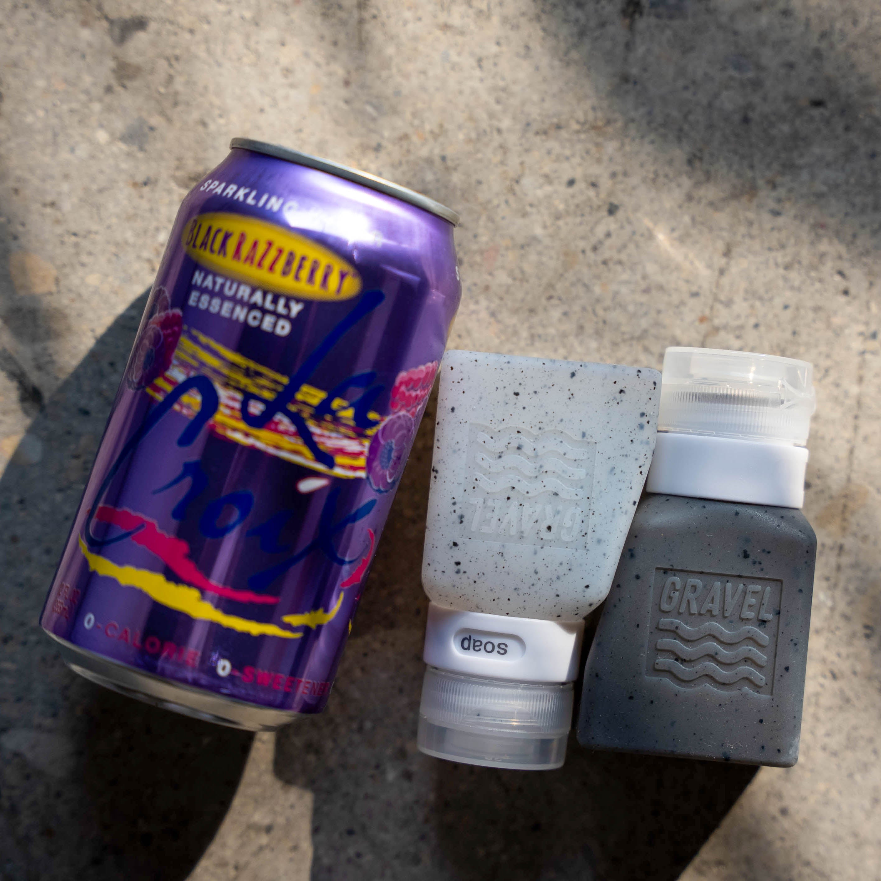 Purple can of Black Kalzberry sparkling water with two gray containers on a concrete surface.