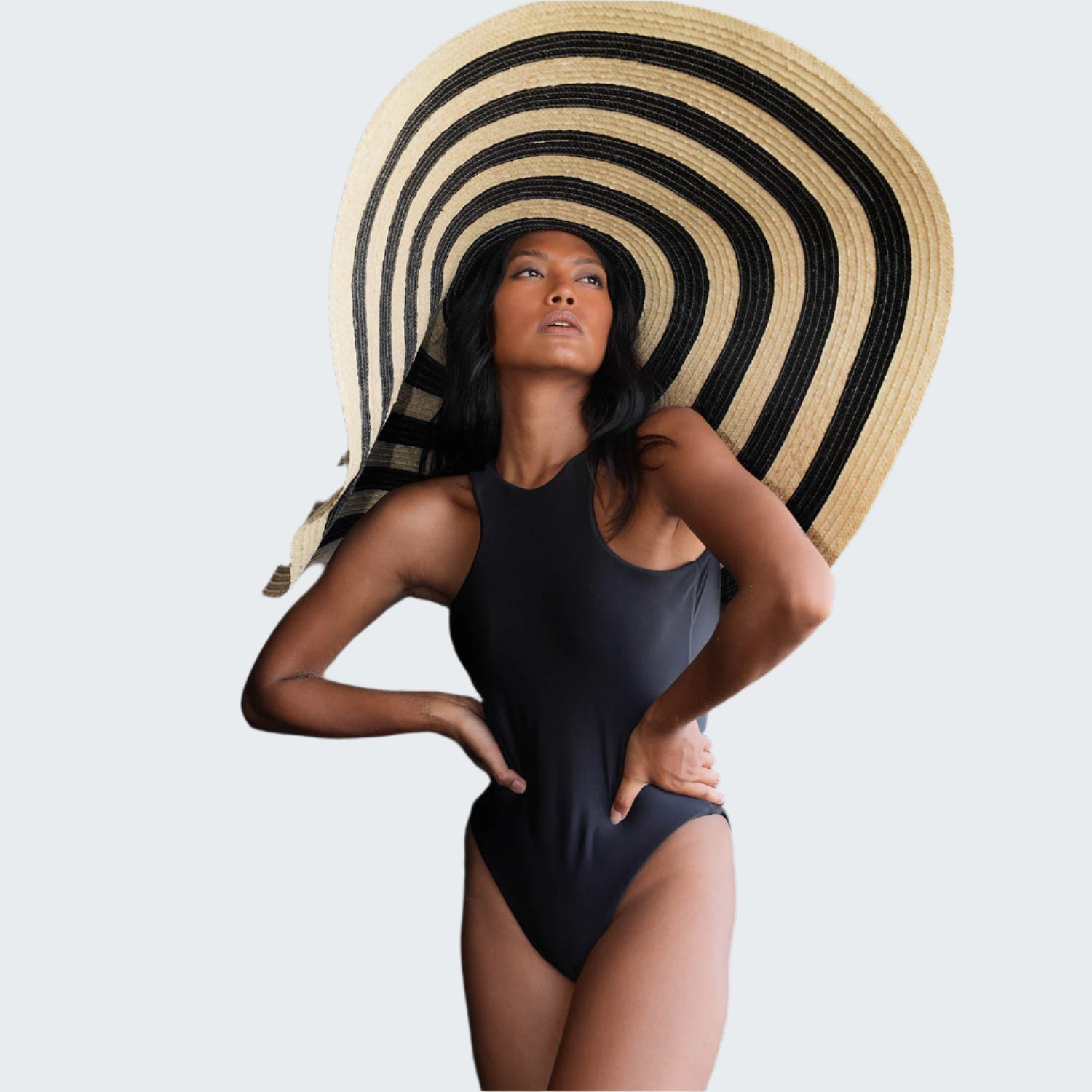 Woman wearing a black swimsuit and large sun hat against a rocky background