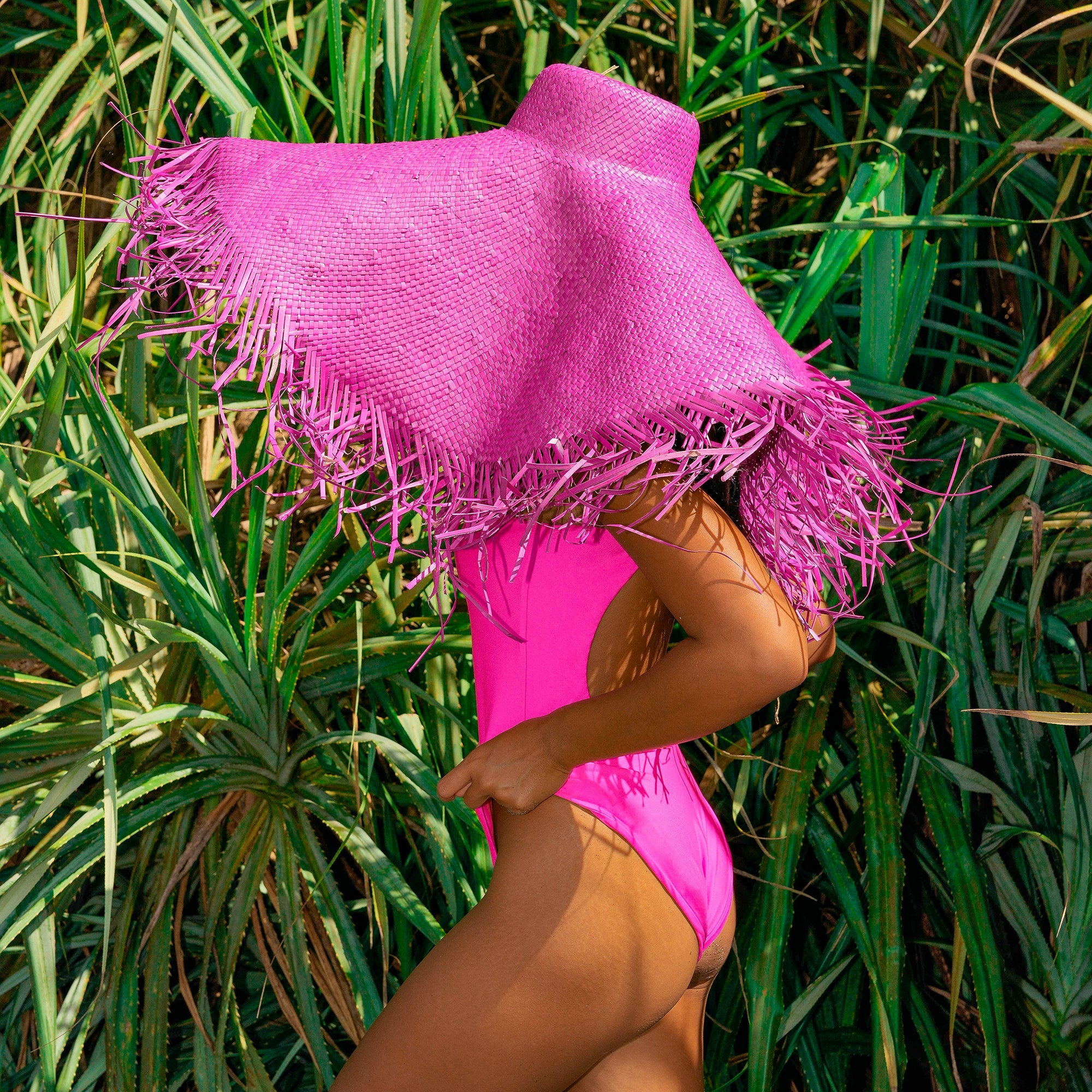 Person wearing a bright pink swimsuit with a matching pink hooded cover-up in a grassy area.
