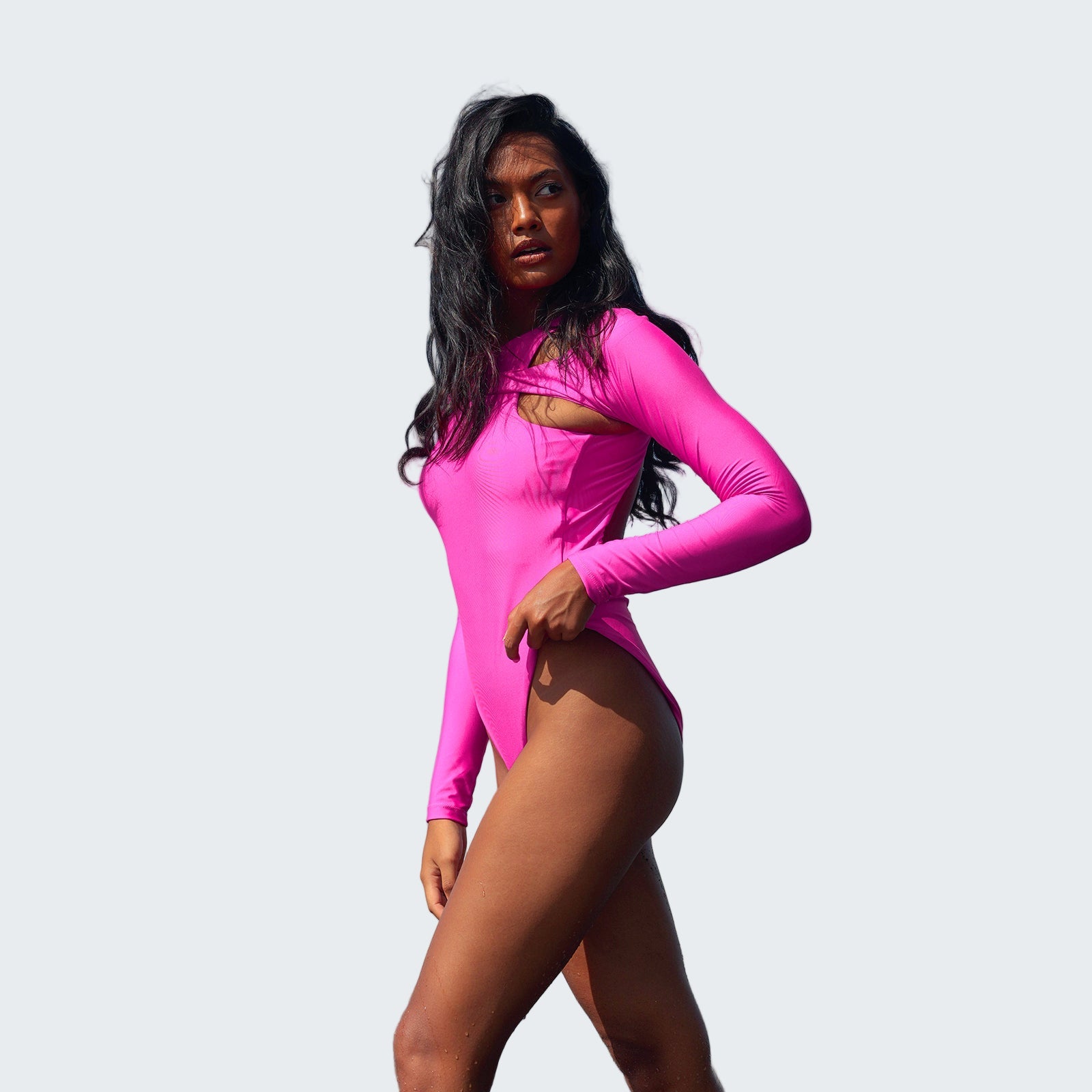 Woman in a bright pink swimsuit standing on a beach with clear blue sky.