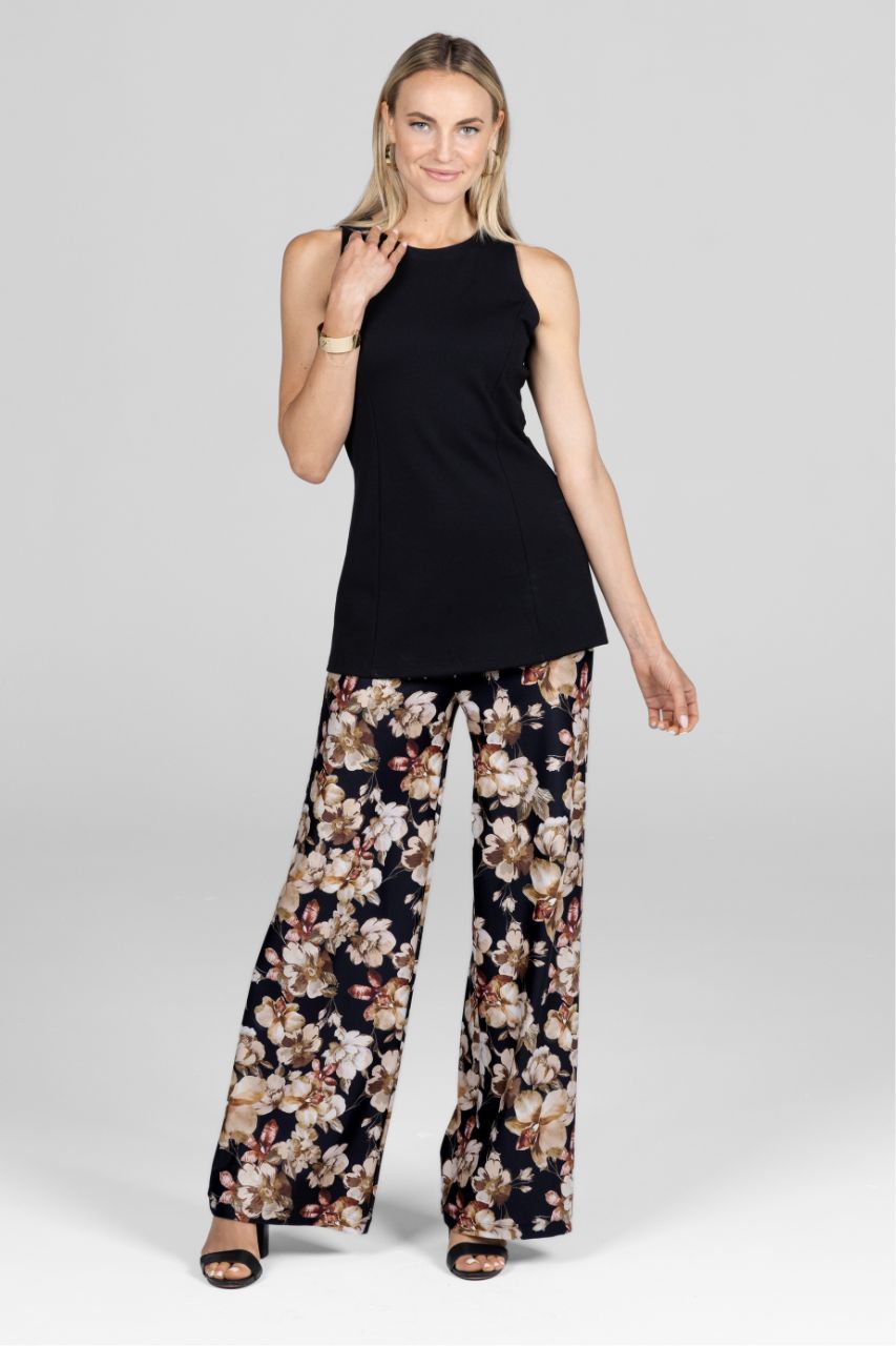 Woman wearing a black sleeveless top and floral pants on a gray background