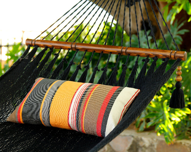 Black hammock with a striped pillow against a green leafy background
