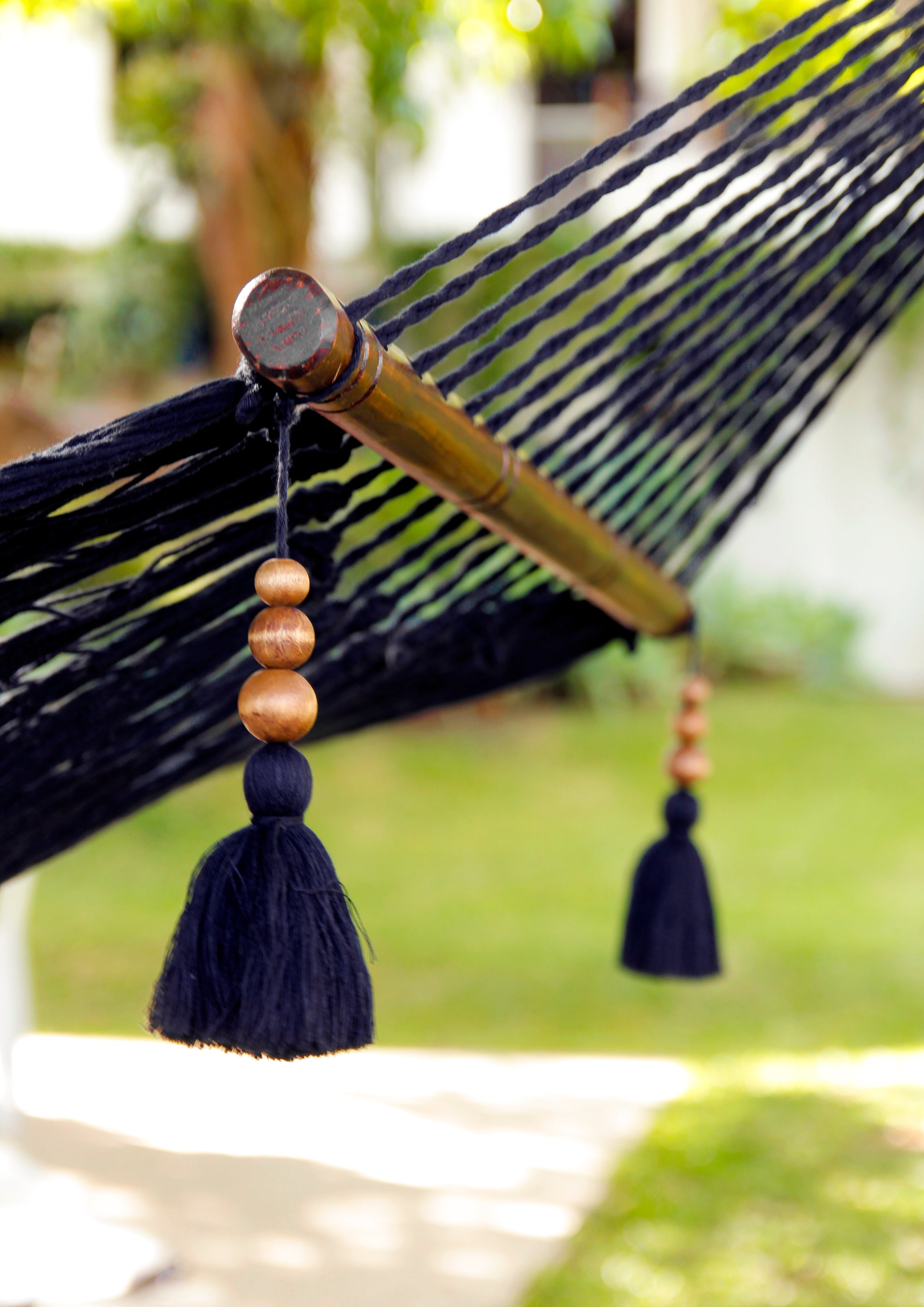 Close-up of a black hammock with wooden beads and tassels, blurred green background