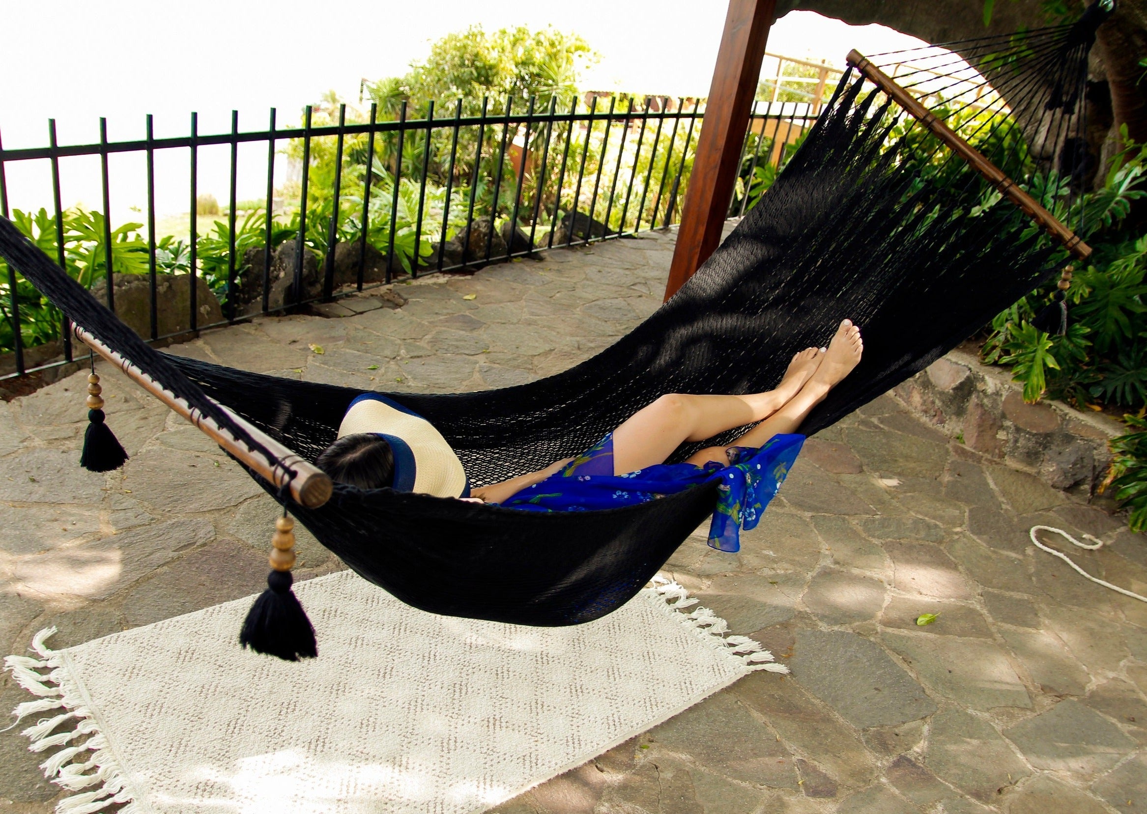 Person lying in a black hammock on a stone patio with greenery in the background