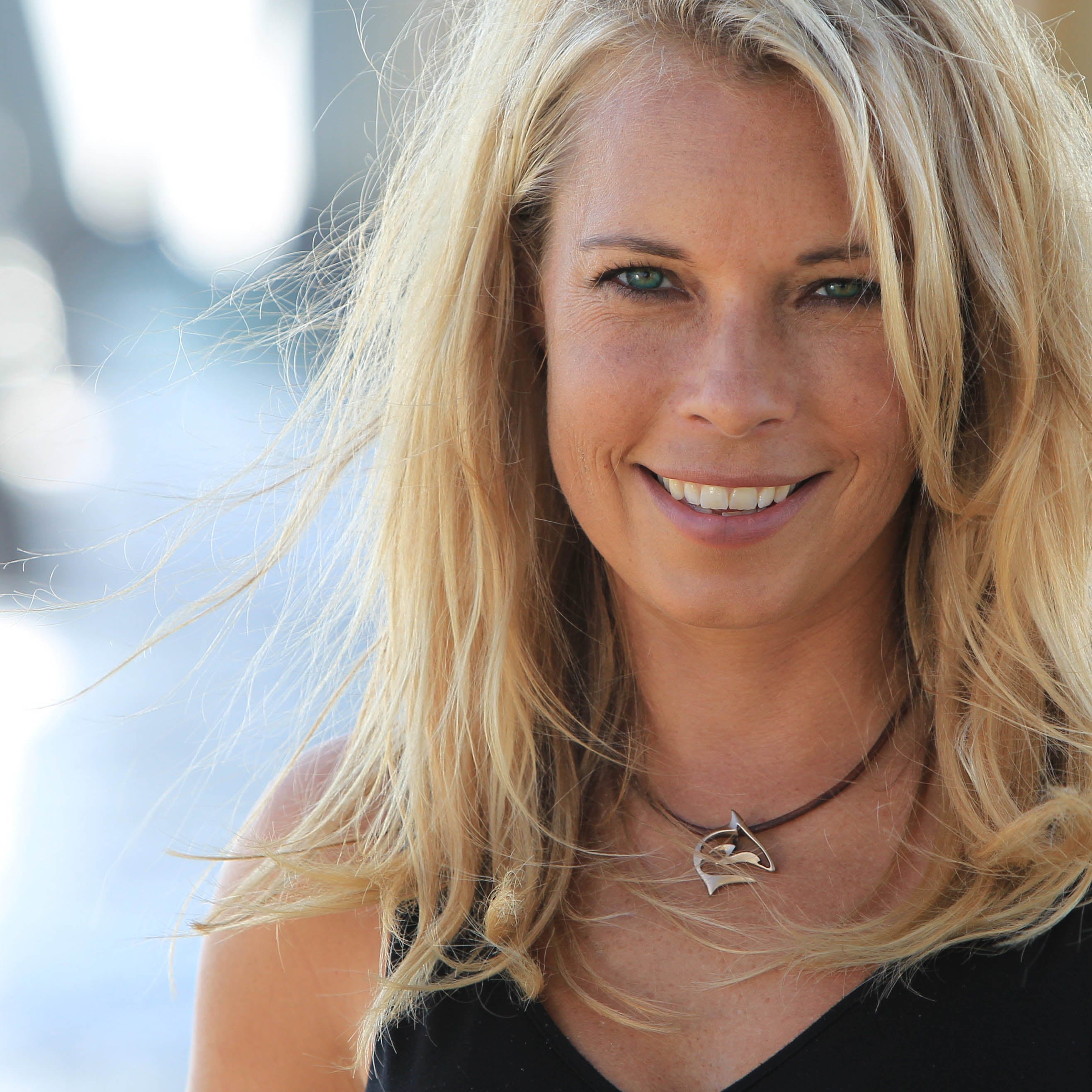 Woman with blonde hair and a necklace, smiling outdoors