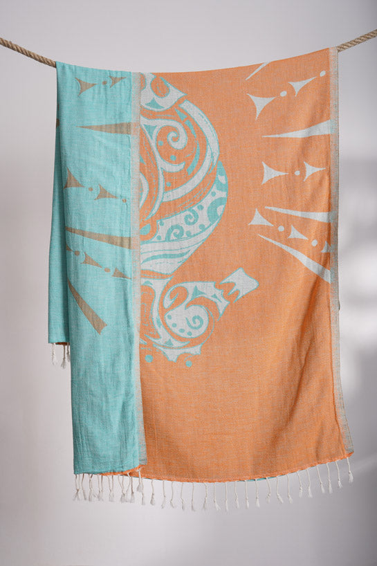 Two scarves with decorative patterns, one turquoise and one orange, hanging on a rope against a neutral background.