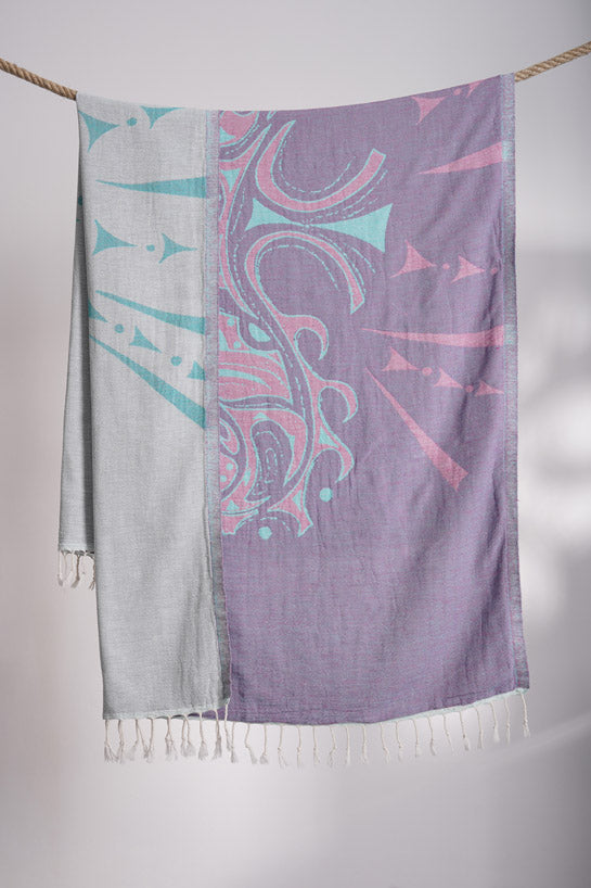 Two patterned scarves, one gray and one purple with pink and blue designs, hanging on a rope against a white background.