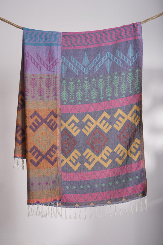 Colorful patterned scarf with geometric designs hanging on a rope against a neutral background