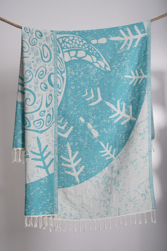 Teal and white patterned towel with fringes on a gray background