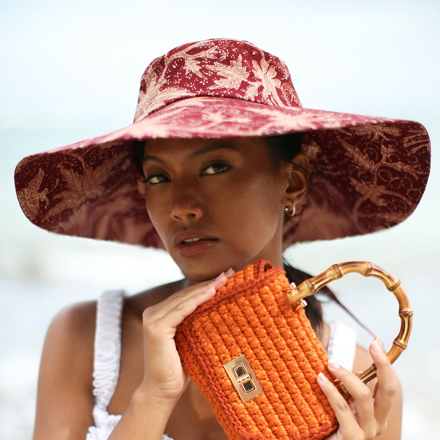 Woman wearing a red floral sun hat and holding an orange handbag with a blurred background