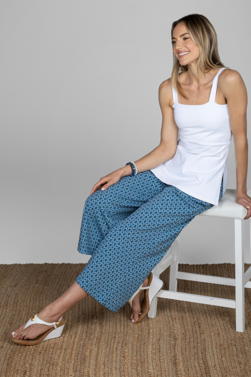 Woman sitting on a chair wearing a white tank top and blue patterned pants.