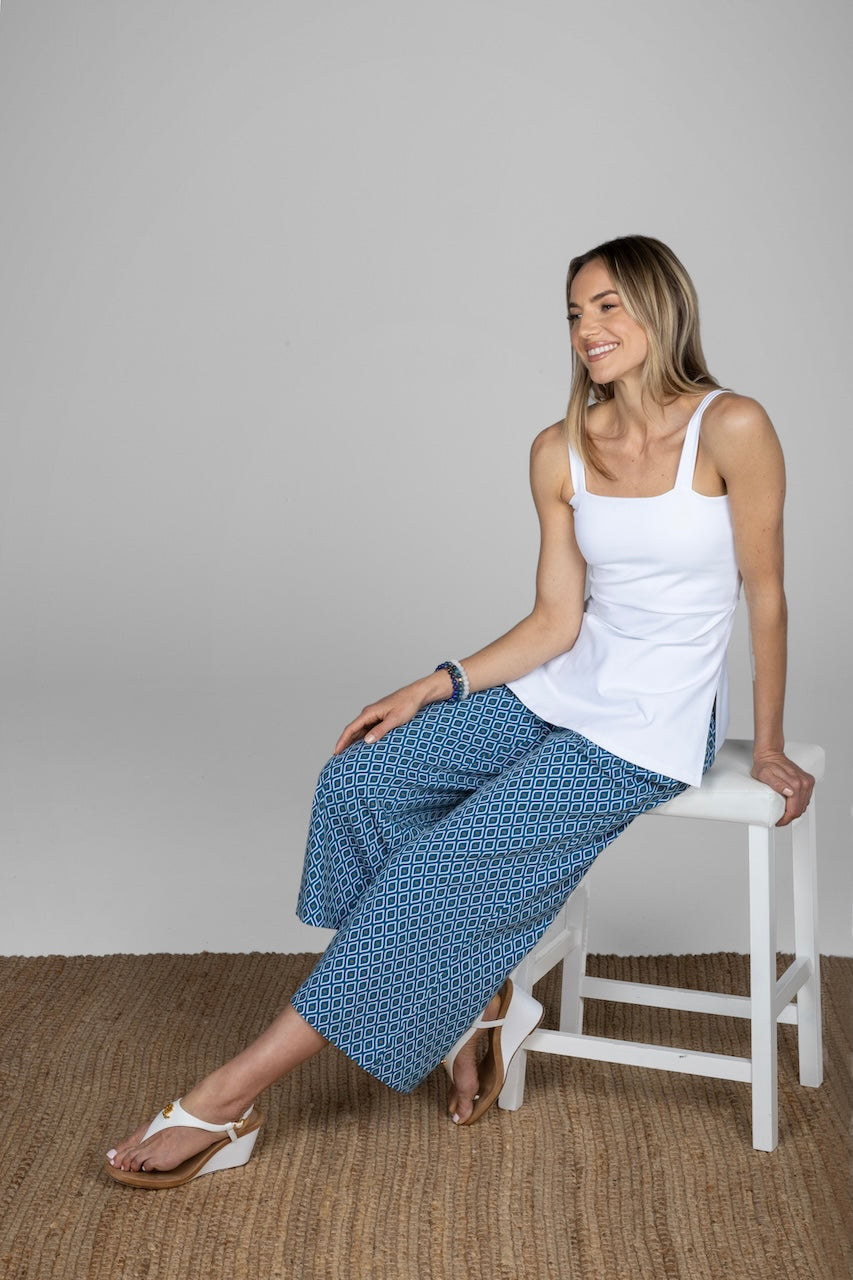 Woman sitting on a chair wearing a white tank top and blue patterned pants.