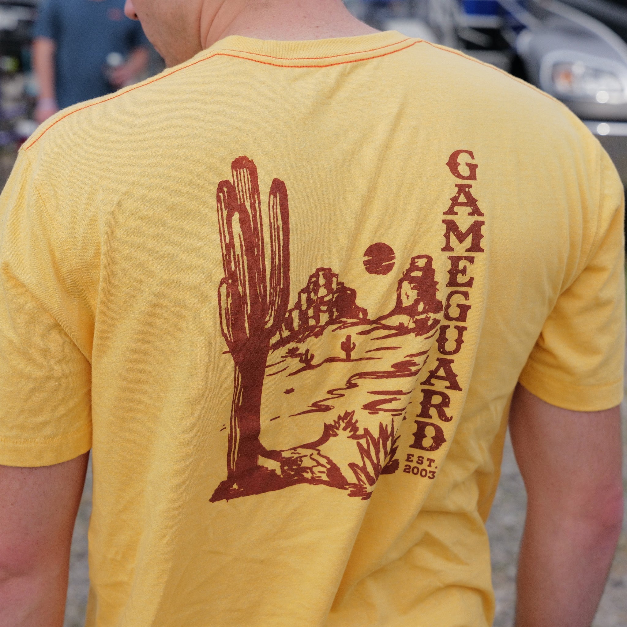 Yellow t-shirt with a desert-themed graphic and 'GameGuard' text on the back.