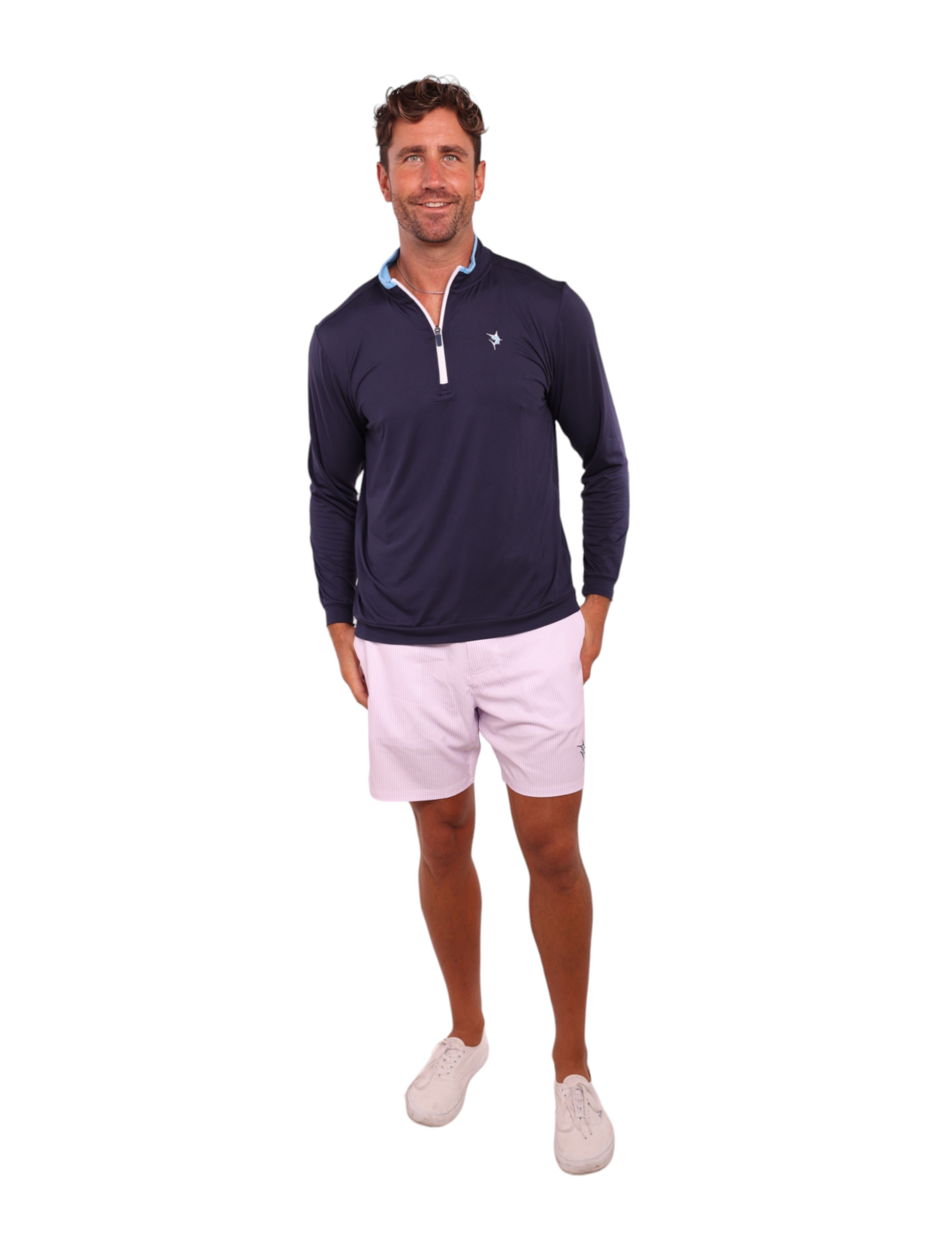 Man wearing a navy long-sleeve shirt with a logo and light pink shorts on a white background