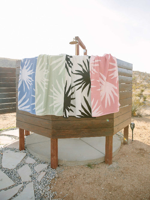 Four colorful towels hanging on a wooden rack outdoors.