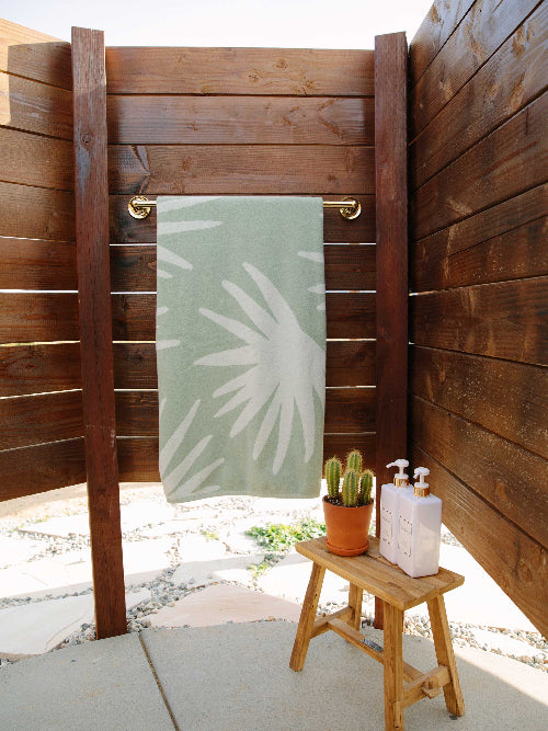 Outdoor shower area with a towel, cactus, and soap on a wooden stool.