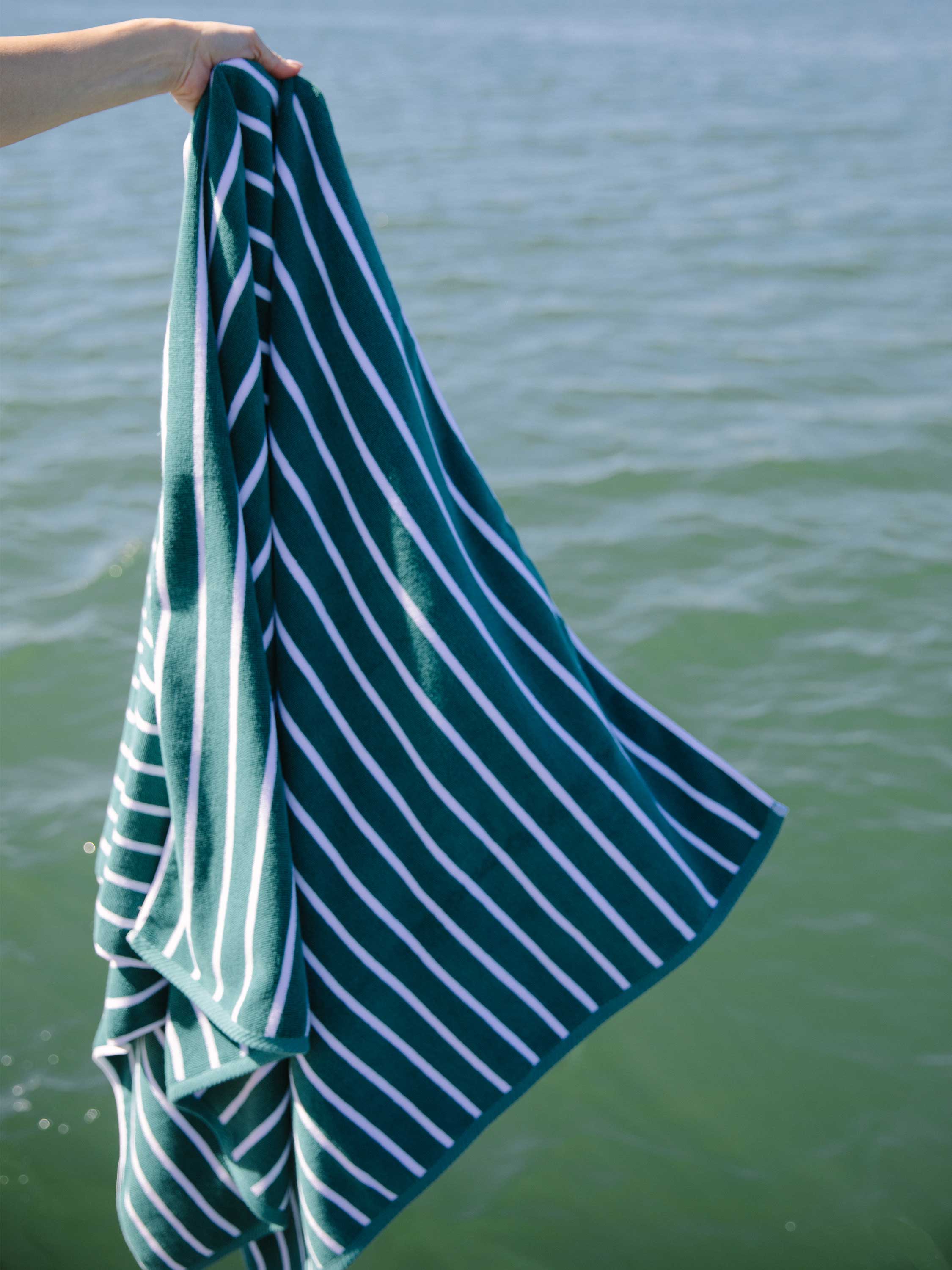Person holding a green and white striped towel by water