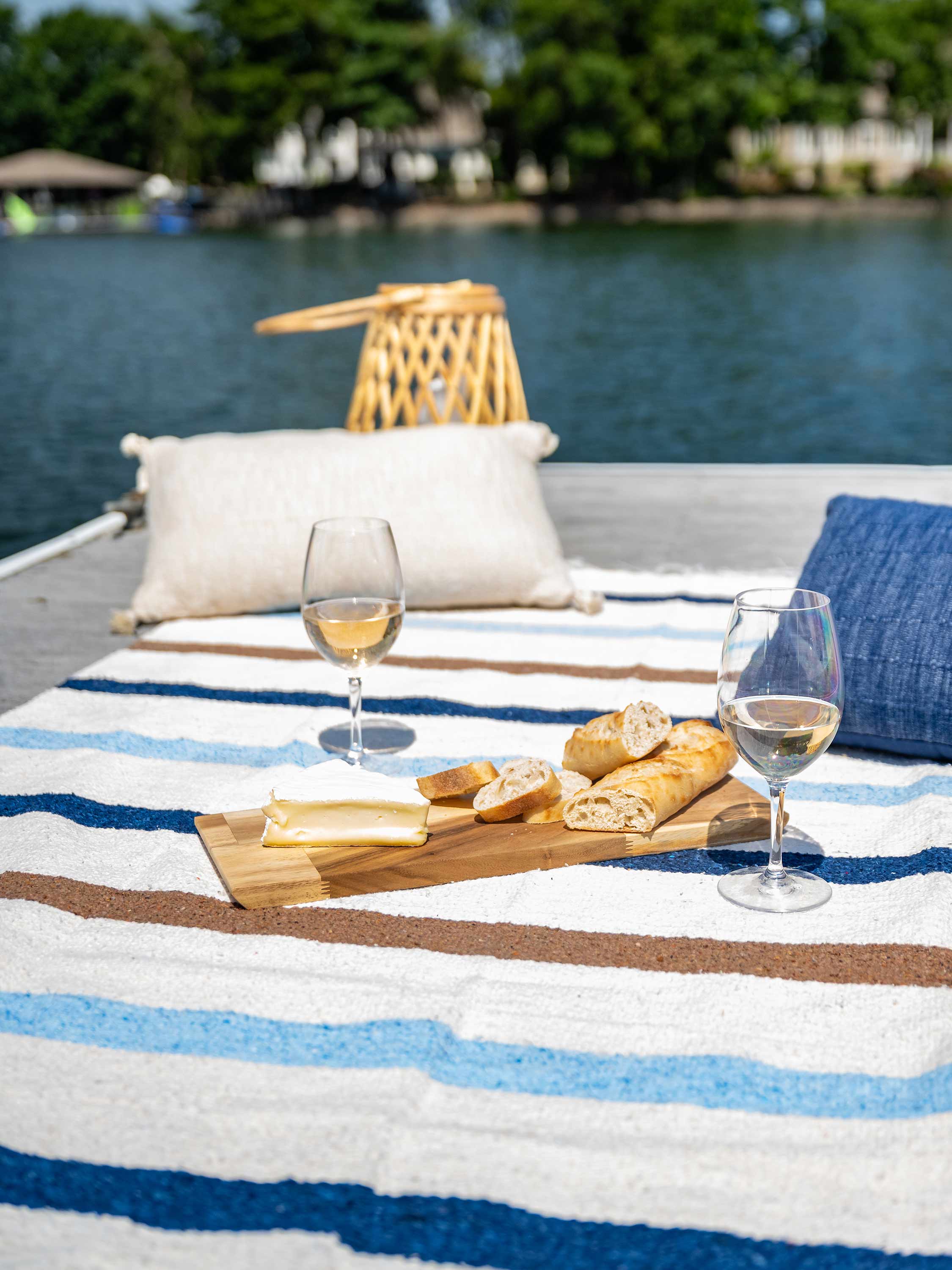 Outdoor setting with a striped blanket, bread, and wine on a dock by water.