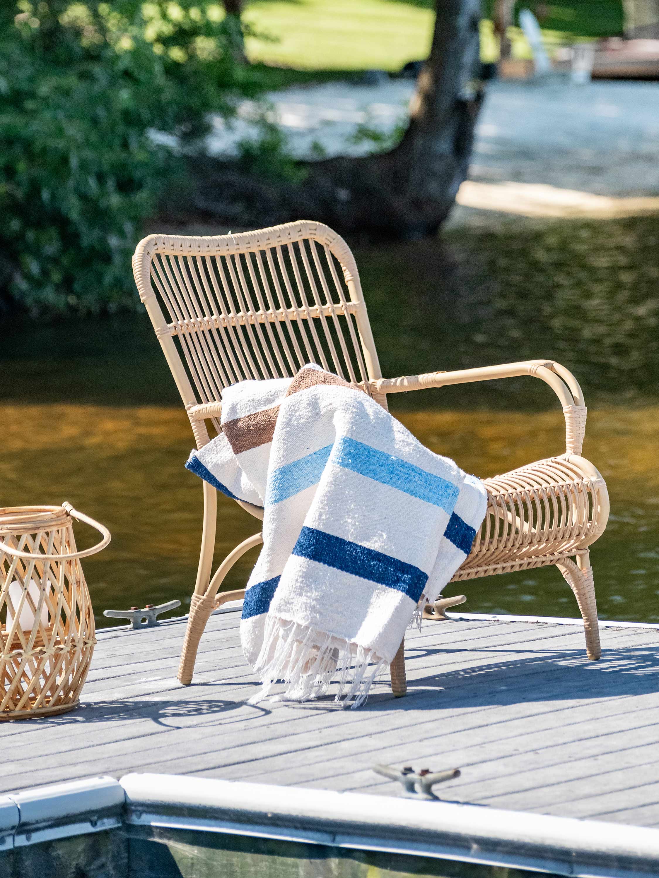 Wicker chair with a striped towel on a dock by a body of water