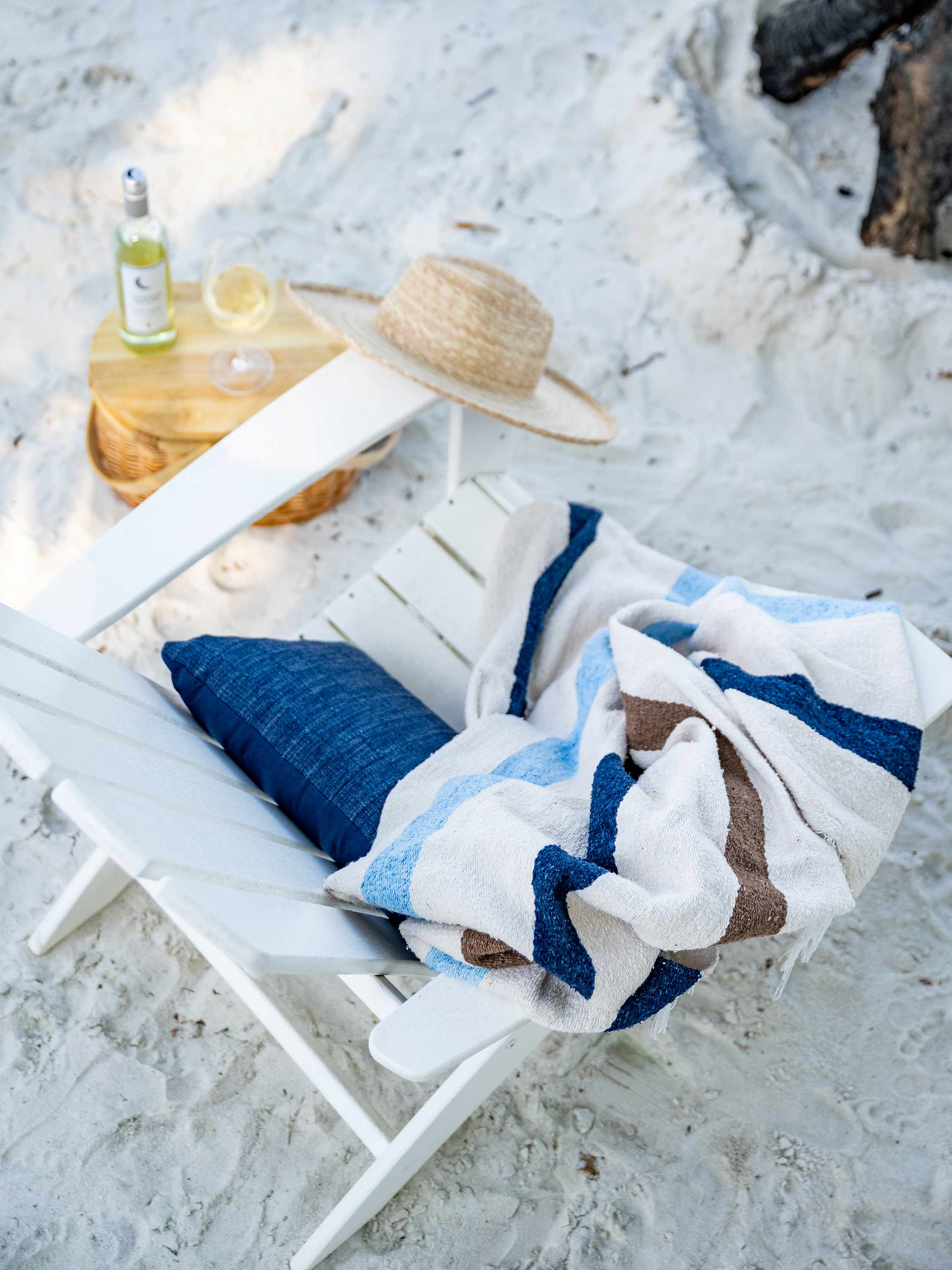 Beach chair with striped towel, hat, and bottle on sand
