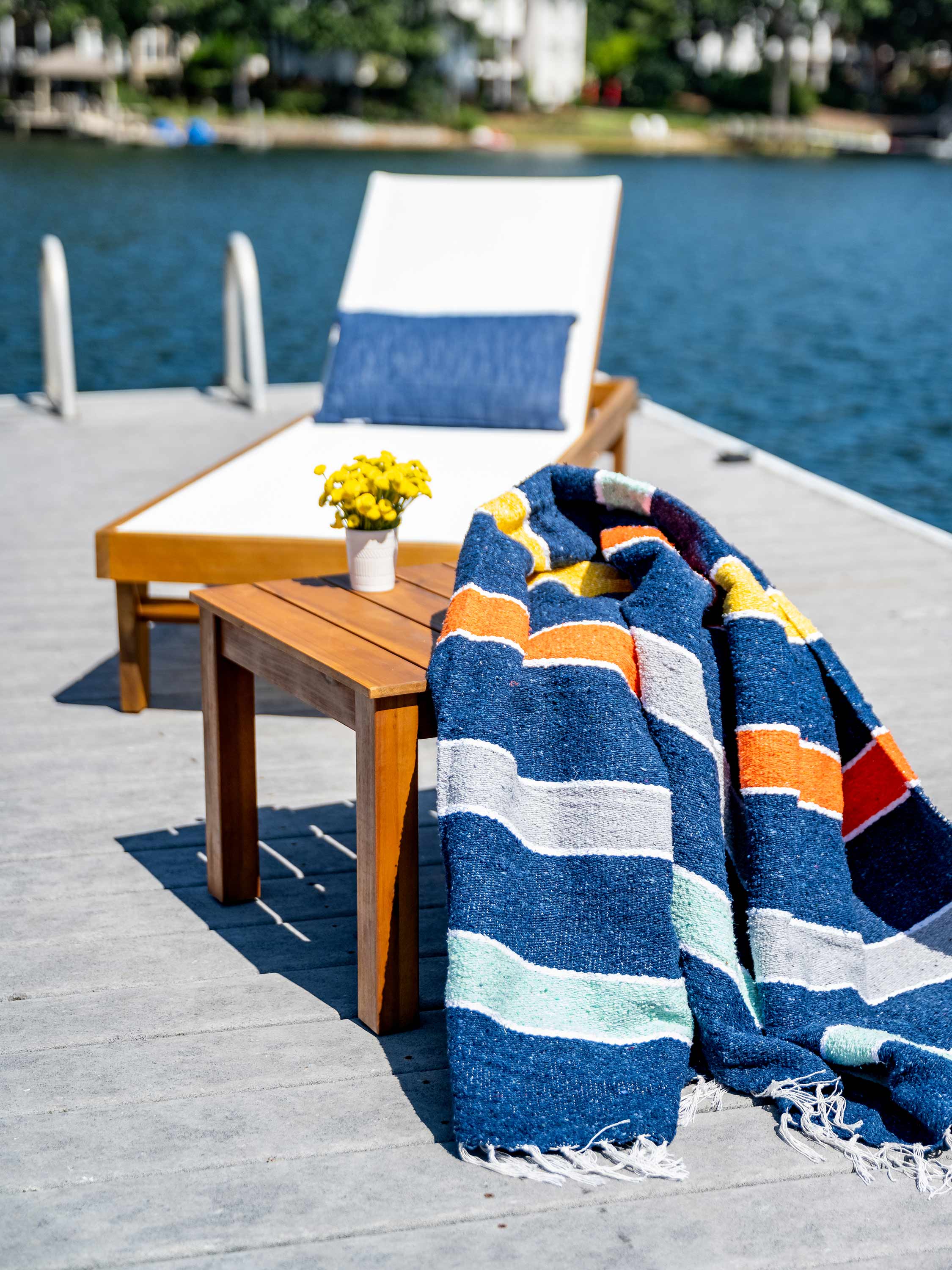 Striped towel draped over a wooden table on a dock with water and chairs in the background
