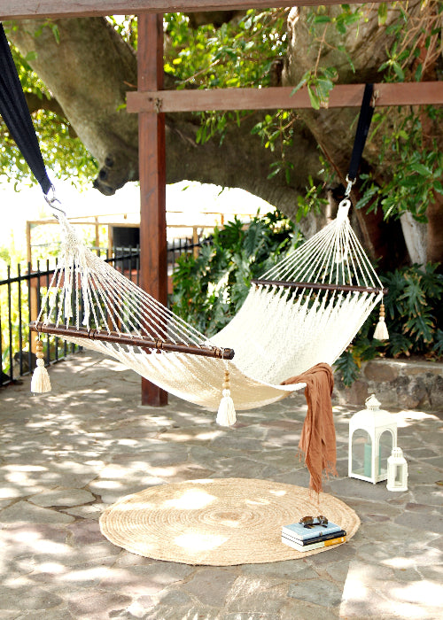Hammock hanging between trees on a patio with a round mat and books below